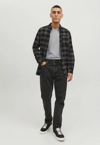 Camicia di flanella a quadri neri e grigi sovrapposta a una maglietta grigia, abbinata a jeans neri e scarpe sportive nere con suole bianche.
