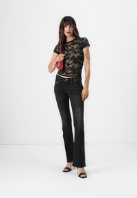 Μαύρη δαντελένια μπλούζα συνδυασμένη με εφαρμοσμένα μαύρα τζιν. Το σύνολο διαθέτει σφιχτή σχεδίαση και συμπληρώνεται από μαύρες γόβες με λουριά και μια κόκκινη τσάντα.