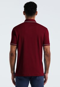 Polo en bourgogne à manches courtes, doté d'un col classique et d'accents blancs contrastants sur le col et les manches.