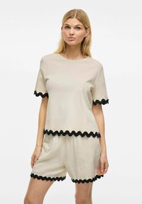 Beige set van een kortemouwtop en shorts met zwarte gekartelde trim. Zacht, lichtgewicht materiaal; casual pasvorm, ronde halslijn.