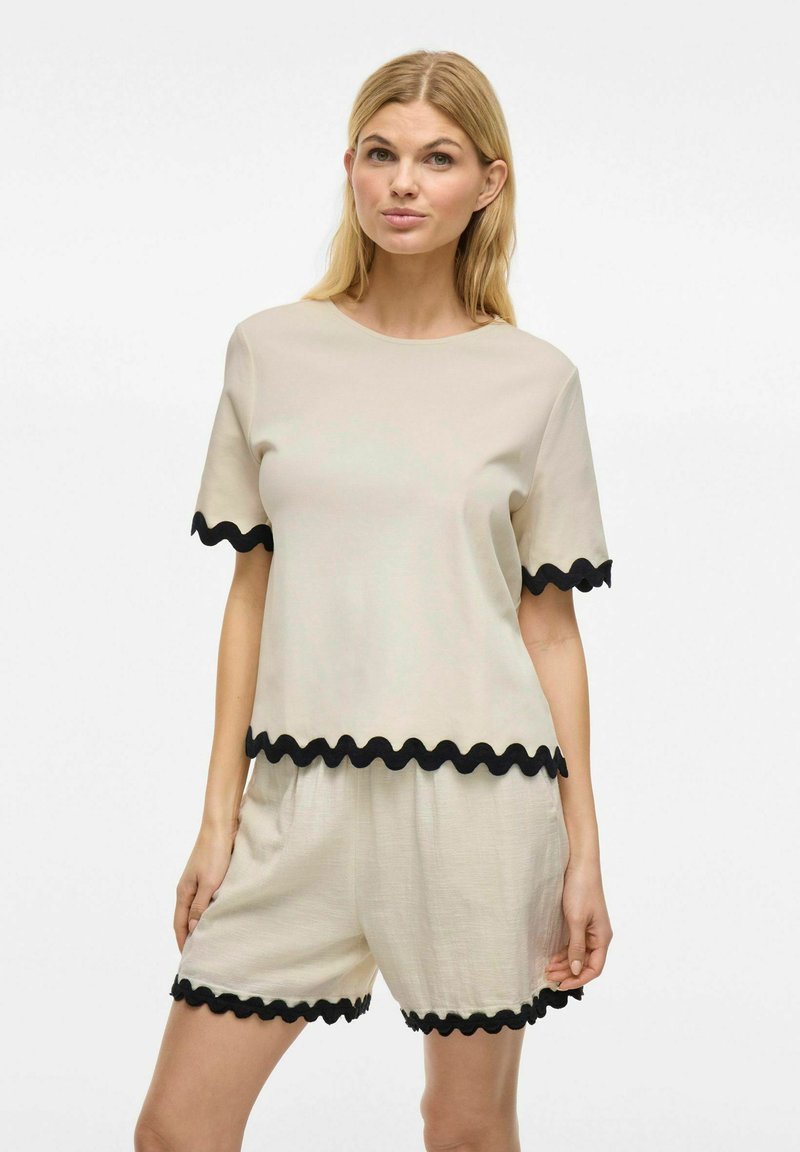 Beige set van een kortemouwtop en shorts met zwarte gekartelde trim. Zacht, lichtgewicht materiaal; casual pasvorm, ronde halslijn.