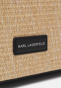 Gros plan sur un tissu beige tissé avec une étiquette rectangulaire noire cousue, affichant « KARL LAGERFELD » en lettres majuscules blanches.