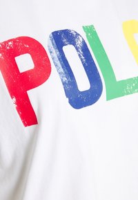 Vit bomull t-shirt med djärva, slitna bokstäver som stavar "P O L O" i röd, blå, grön och gul färg.