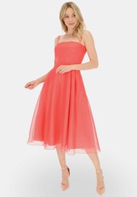 Koralowa, bezrękawna sukienka midi z dopasowaną górą i rozkloszowanym, zwiewnym dołem. Lekki, przezroczysty materiał o subtelnej fakturze.