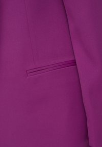 Gros plan d'une poche de blazer magenta avec une ouverture passepoilée, montrant une texture de tissu lisse et des détails de coutures.
