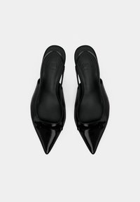 Sapatilhas slingback de verniz preto, com bico apontado e um pequeno detalhe de fivela, sobre um fundo branco.