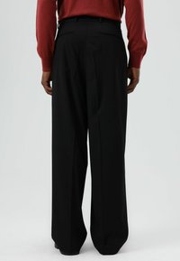 Zwarte brede pijpen broek met een gladde textuur, met plooien, zijzakken en een getailleerde pasvorm, gezien vanaf de achterkant.