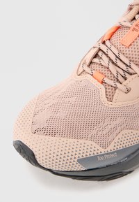 Light pink athletic shoe with a mesh upper, textured patterns, orange accents, and a gray rubber outsole labeled "Toe Protect."