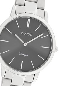 Montre-bracelet en acier inoxydable argenté avec un cadran gris rond, des marqueurs d'heure index minimalistes et le texte "OOZOO Vintage" en blanc.