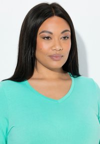 Maglietta turchese con scollo a V in tessuto morbido e liscio. Presenta maniche corte e una vestibilità comoda. Primo piano dello scollo e del volto.