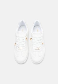 Baskets blanches en cuir lisse, avec des accents texturés, des éléments dorés et des lacets plats. Design épuré au style minimaliste.