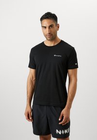 Black short-sleeve T-shirt made of cotton, featuring a white Champion logo on the left chest and a sleeve logo, with a crew neckline.