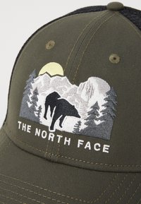 Boné verde-oliva com um design bordado apresentando um urso, montanhas e árvores. Logótipo bordado "THE NORTH FACE" em branco na parte da frente.
