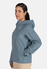 Chaqueta impermeable de color azul claro con capucha, que cuenta con cierre de cremallera y bolsillos laterales. Textura suave y diseño de tejido transpirable.