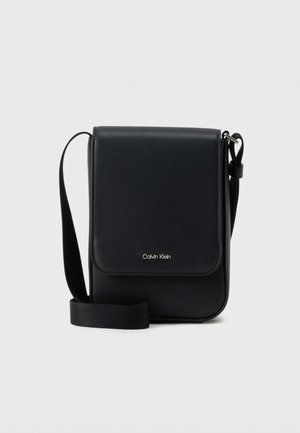 Sacoche Calvin Klein noire avec rabat, bandoulière ajustable et petit logo doré à l'avant, sur fond blanc uni.