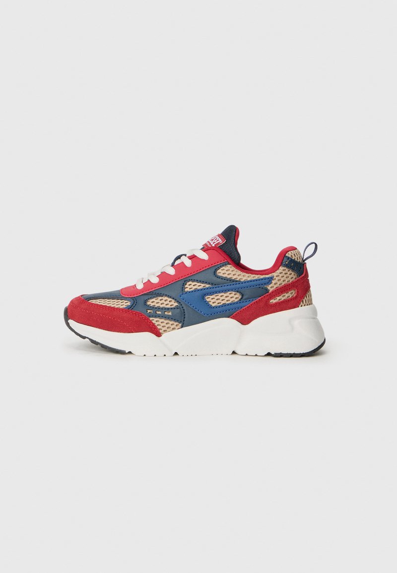 Zapatilla deportiva de malla en rojo, azul y beige, con cordones blancos y suela gruesa blanca, mostrada de lado sobre un fondo blanco.