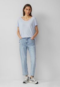 Jasnoniebieska koszulka typu V-neck zestawiona z jasnoniebieskimi spodniami o wysokim stanie i srebrnymi sneakersami. Stylizacja ma luźny krój i casualowy charakter.