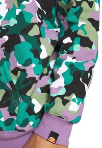 Sudadera de camuflaje verde y púrpura, con un puño ribeteado en púrpura, tejido texturizado y una pequeña etiqueta de logo en la manga.