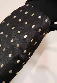 Fekete szoknya textúrált felülettel, aranyfóliás pöttyökkel díszítve. A dizájn szoros derékbőséget és folyó sziluettet tartalmaz.