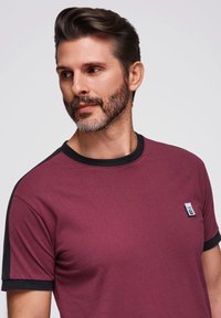 Bordová pánská tričko s krátkým rukávem a černými akcenty na límci a rukávech. Obsahuje malou nášivku s logem na levé hrudi. Měkký bavlněný materiál.
