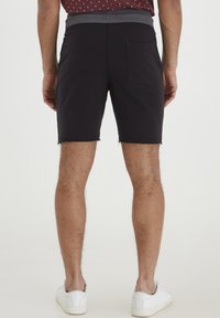 Zwarte katoenen shorts met een grijze elastische tailleband, een raffelzoom en een enkele achterzak, gecombineerd met witte sneakers.