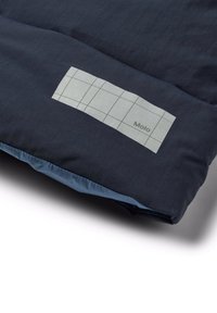 Laivastonsininen makuupussi, jossa on harmaa suorakulmainen etiketti, jossa on ruudukkomuotoilu ja teksti "Molo". Rakenteellinen pinta, jossa on sileä reuna.