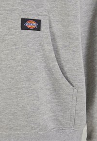 Szürke pulóver anyag texturált felülettel. Elöl egy zseb található, valamint egy fekete Dickies címke színes logóval.