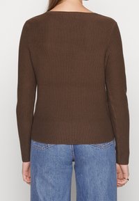 Top marron à manches longues avec un col rond et une silouhette ajustée, complété par un tissu texturé et un ourlet droit.