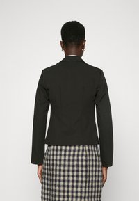 Černý přizpůsobený blazer s těsným střihem, dlouhými rukávy a klopami, doplněný kostkovanou sukní v krémových a námořnických odstínech.