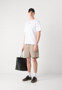 Maglietta bianca a maniche corte, pantaloni beige, borsa a tracolla nera in pelle, sneakers grigie con calzini bianchi e un cappellino nero. Outfit semplice e casual.