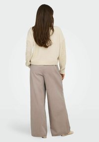 Cremefarbener Strickpullover mit kunstvoll gemusterten Ärmeln, kombiniert mit locker sitzenden, weit geschnittenen Hosen in hellem Taupe. Strukturierte, entspannte Passform.