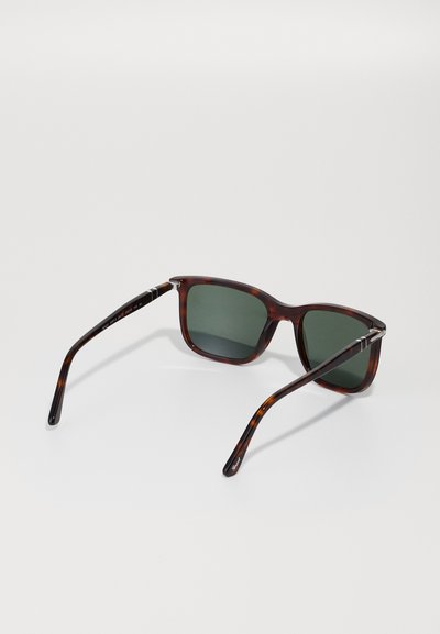 Óculos de sol tartaruga com lentes verdes. Design de armação quadrada, textura suave e hastes elegantes com discretos detalhes prateados nas dobradiças.