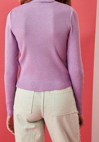 Haut à manches longues côtelé de couleur lilas clair avec un col montant, accompagné d'un jean clair avec un ourlet effiloché et des poches arrière.