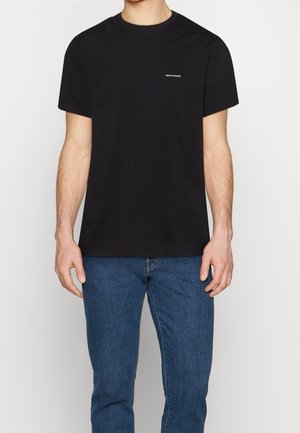 Czarna bawełniana koszulka z krótkim rękawem, okrągłym dekoltem i małym logo na piersi. Połączona z niebieskimi dżinsami.