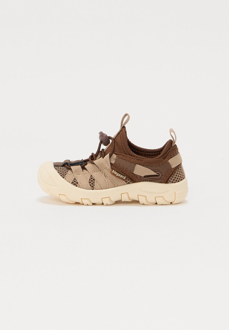 Ruskeat urheilukengät, joissa on verkkopaneelit, kumipohjat ja joustavat nauhat. Varustettu sileällä beigeellä kärjellä ja tekstuuripinnoilla päällisessä.