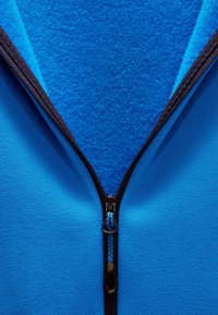 Blauwe zip-up jas met een gladde buitenstof en een zachte fleece binnenkant. Zwarte rits met blauwe accenten in het midden.