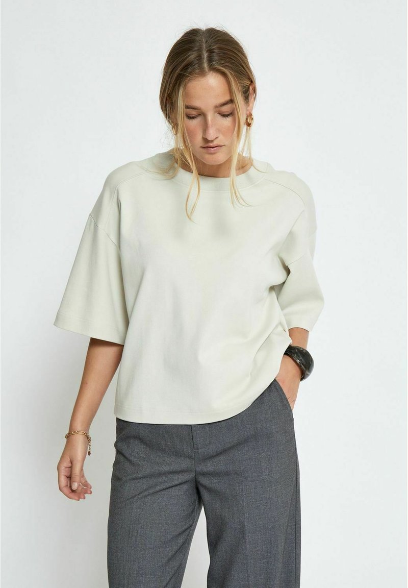 Light gray oversized short-sleeve top with a round neck, soft texture, and relaxed fit, paired with gray tailored trousers.