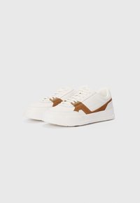 White sneakers with brown suede accents, featuring a textured finish, lace-up design, and a thick, solid-colored rubber sole.