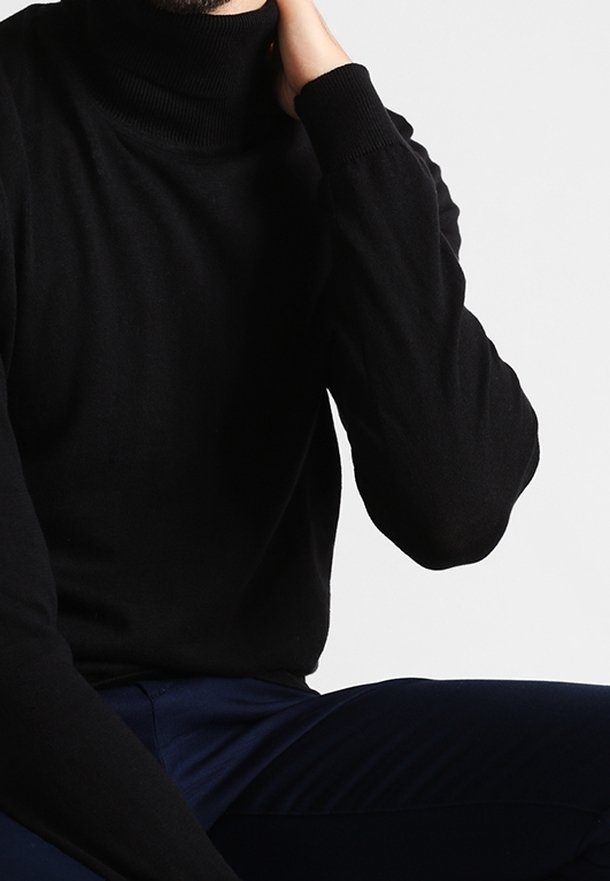 Czarny sweter z wysokim kołnierzem, z ribbowanym wykończeniem i długimi rękawami, wykonany z miękkiego materiału. Noszony z ciemnoniebieskimi spodniami.