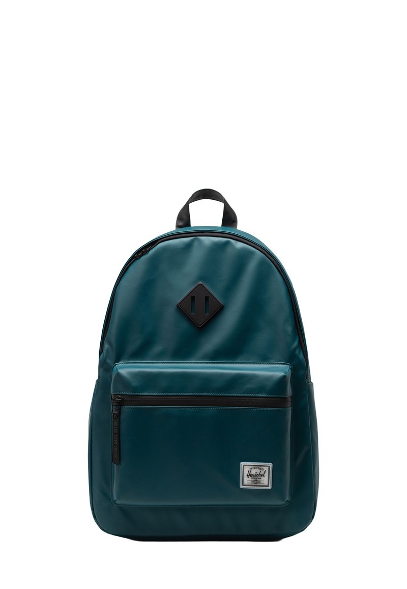 Türkisfarbener Rucksack mit glatter Oberfläche, schwarzen Reißverschlussakzenten, einer Fronttasche und einem diamantförmigen Lederpatch auf der Vorderseite.