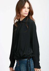 Blusa nera a maniche lunghe con colletto e vita stretta. Realizzata in tessuto morbido, presenta jeans con bottoni e una vestibilità rilassata.