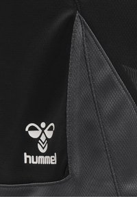 Tejido atlético negro con un acento gris texturizado. Presenta un logo blanco con una abeja estilizada. Material suave y transpirable.
