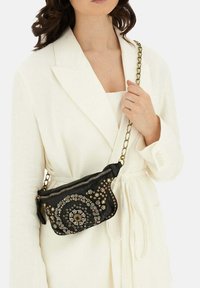 Zwarte leren pouch tas versierd met meerkleurige edelstenen in een circulair patroon, met een gouden kettinghengsel en rits sluiting.