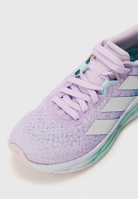 Purple athletic shoe with textured mesh upper, light green accents, white three-stripe logo, and a cushioned sole. Laces included.
