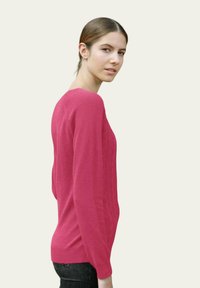 Pull en tricot rose avec un col rond, des poignets côtelés et un motif texturé. Coupe ajustée, associé à un jeans foncé, présenté de côté.