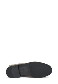 Zapato de gamuza marrón con una suela de goma negra. La suela presenta un patrón texturizado y tiene un pequeño tacón. Etiqueta impresa en el interior.