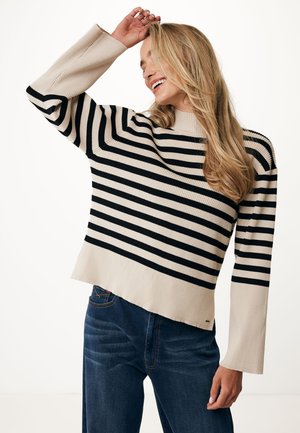 Gestreepte trui in beige en zwart, ribbelmateriaal, hoge kraag, brede mouwen en een ontspannen pasvorm, gecombineerd met donkerblauwe jeans.