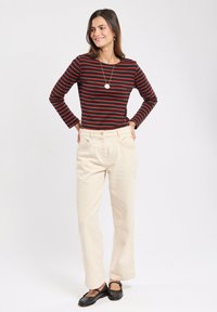 Maglietta a maniche lunghe a strisce in nero e rosso, abbinata a pantaloni a gamba larga beige a vita alta e scarpe basse nere. Dettaglio con collana semplice.