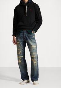 Felpa nera con cappuccio e cordini crema, abbinata a jeans blu slavati con toppe e dettagli sfrangiati. Indossate sneaker bianche.