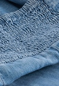 Tissu bleu clair présentant une texture froncée en haut, des sections lisses en dessous, et une finition en tricot douce avec un éclat subtil.